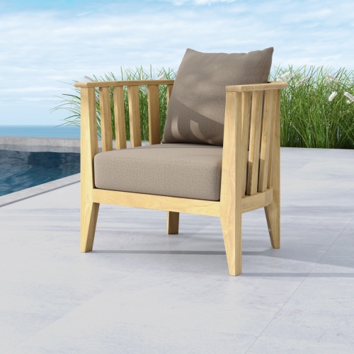 12170DP Kafelonia teak Barrel Chair angled front view on patio next to a pool with landscape plants and blue sky background 