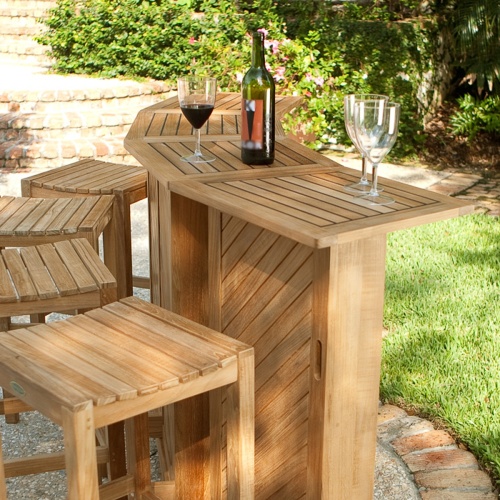 70084 somerset teak bar set fully opened showing three wine glasses and wine bottle on bar top displayed on patio with potted plants stone steps vegetation in background 