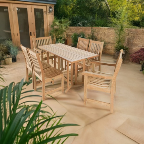 70165 Nevis Veranda 7pc Teak Dining Set in angled aerial view on a stone patio surrounded by plants in front of French doors and a brick privacy fence with trees in the background