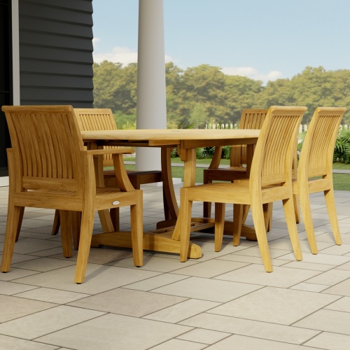 70363 Martinique Laguna 7 pc Dining Set of Martinique Teak Oval Table and 2 Laguna Dining Armchairs and 4 Laguna Side Chairs angled end view on tile patio with a pillar and trees in background