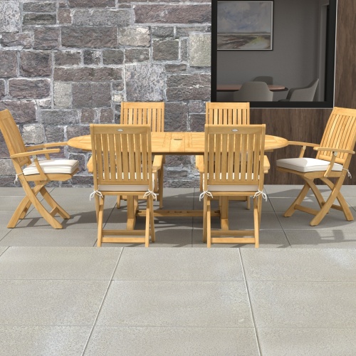 70368 Oval Barbuda Chair 7 pc Dining Set of Martinique Oval Table and 6 Barbuda Teak Arm Chairs in side view on outdoor patio with stone house and glass sliding doors in the background