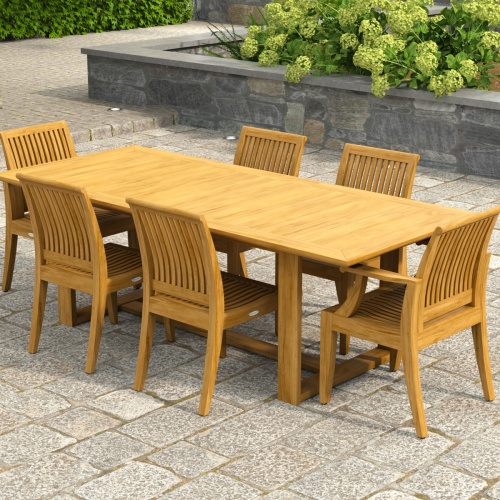 70377 Horizon Laguna 7 pc Teak Dining Set of Horizon Dining Table and 2 Laguna DIning Arm Chairs and 4 Laguna Side Chairs on paver patio with raise flower bed with landscaping plants in the background