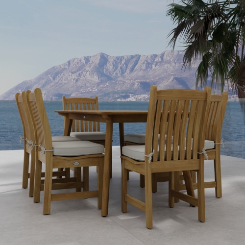 70385 Veranda Horizon 7 pc Dining Set of Surf Rectangular Dining Table and 6 Veranda Side Chairs with optional seat cushions on stone patio with tree and hills and ocean background 