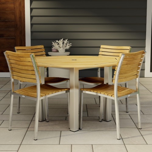 70438 Vogue Dining Set for 4 of Vogue Teak and Stainless Steel 48 inch Round Dining Table and 4 Vogue Stacking Dining Chair angled on patio with a door of house in the background 