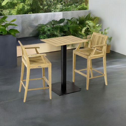 70642  Laguna Barstool 3pc Teak Bar Set of Rectangular Teak Table Top on Black Gar Base and 2 Laguna Barstools angled on outdoor patio with plants and privacy wall and trees in background