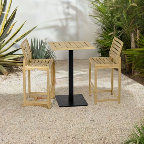 70643 Vogue Somerset 3 pc Barstool Bar Set of Vogue Rectangular teak Table Top on Black Table Base and 2 Somerset Side Barstools angled on stone patio with plants and wall in the background