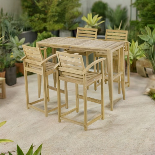 70647 Somerset Laguna Teak Bar Set of Laguna Teak Rectangular Bar Table and 4 Somerset Barstools with arms side angled on a stone patio surrounded by tropical plants and trees in background