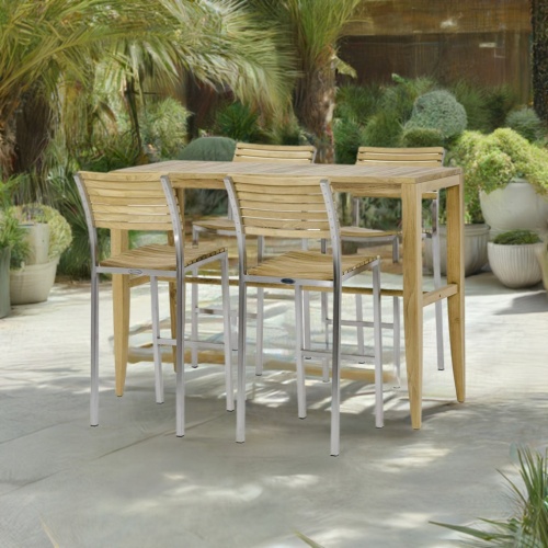 70648 Laguna Vogue Teak Bar Set of Laguna Teak Rectangular Bar Table and 4 Vogue Teak and Stainless Steel Bar Stools angled on stone patio with potted plants and trees in the background