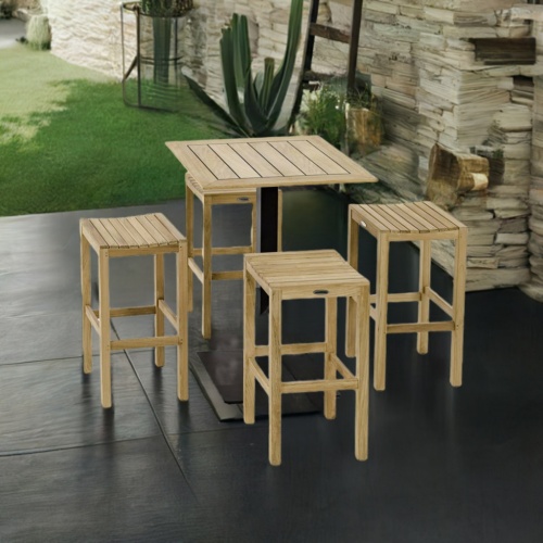 70692 Teak 5 pc High Bar Patio Set angled on a stone patio next to a brick wall with landscape trees and grass in the background