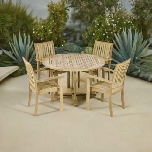 70737 Sussex teak Round Dining Set angled top view with 4 Sussex Teak Armchairs and Teak 48 inch diameter Round Dining Table angled on patio with landscaping plants in the background