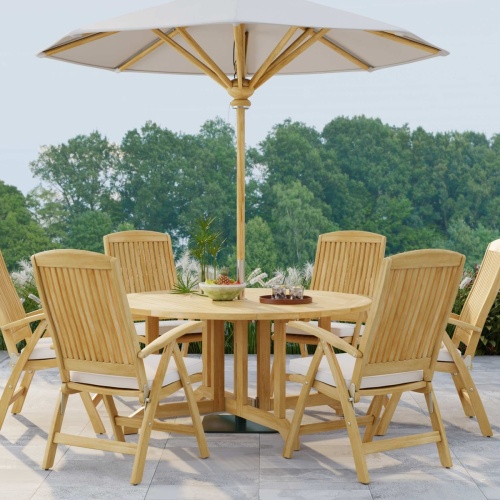 70843 Barbuda Recliner 7 piece Teak Dining Set showing tray with glasses and an optional opened umbrella in side angled view on patio with trees in background