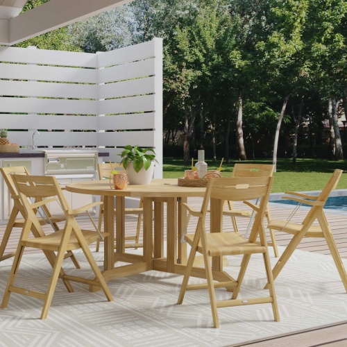 70846 Barbuda Surf 7 piece 60 inch diameter round folding Dining Set with tray drinks and potted plant on patio next to outdoor kitchen and privacy fence angled  view next to pool and trees