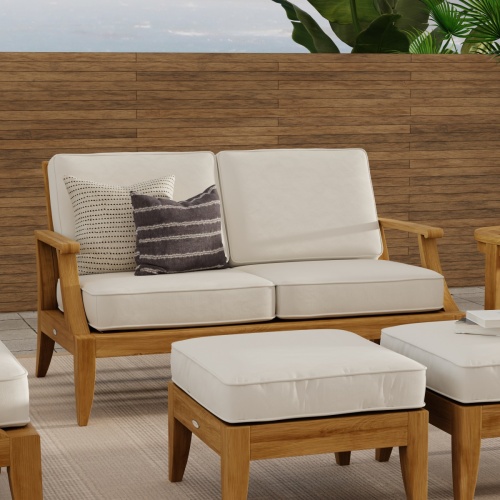 13121DP laguna teak loveseat with cushions and 2 ottomans front angle on patio with privacy wall in the background