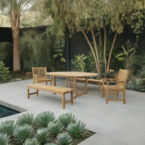 70077 Martinique Veranda Bench and Chair Set of oval extendable teak table and 2 teak armchairs and two 5 foot backless benches side angled on stone patio next to pool with trees along fence in background