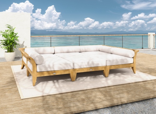 70100 Aman Dais 6 piece teak daybed set with cushions front view on wood deck and stone patio next to potted tree and blue sky and ocean background