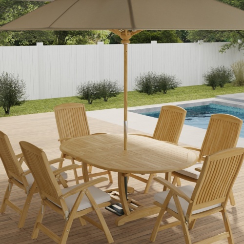 70367 Martinique Barbuda Recliner Dining Set of Martinique Teak Oval Dining Table and 6 Barbuda Reclining dining chairs with optional open umbrella angled on patio next to a pool with plants and fence in background  