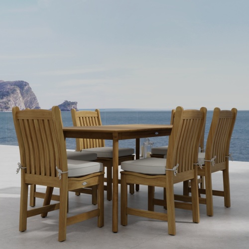 70385 Veranda Surf 7 pc Dining Set of Surf Rectangular Dining Table and 6 Veranda Side Chairs with optional seat cushions angled corner view on stone patio with the ocean in background 