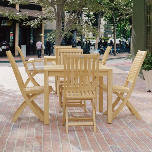 70570 Barbuda 5 pc Dining Set of Barbuda Bistro Teak 36 inch Square Dining Table and 4 Barbuda Folding Chairs side angled view on brick paver courtyard with buildings and trees and people walking in background