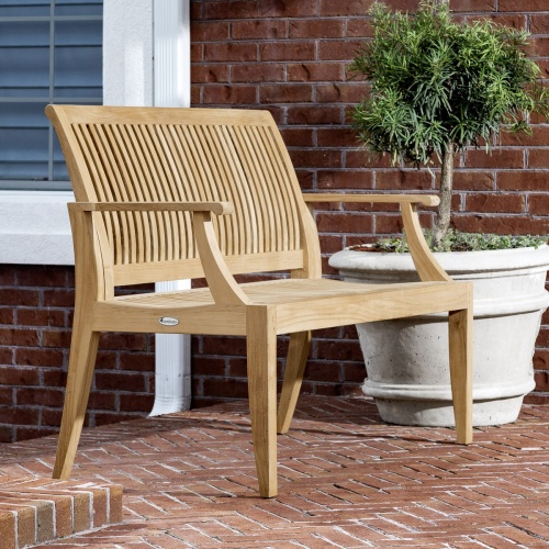 70849 Laguna teak 6 foot long bench angled on brick porch with planted tree in white planter and window and brick wall in background