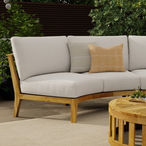 70870 Kafelonia Lounge Sofa 6 pc Set showing partial view of  Kafelonia Sofa Sectional Bench and 2 pillows and Teak Coffee Table angled on patio with shrubs in background