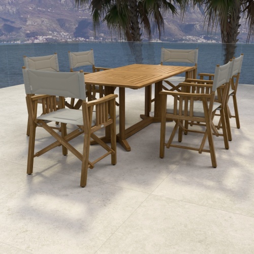 70360 Pyramid Director 7 piece teak Dining Set of 6 teak Director Chairs and Pyramid Teak Dining Table end view on stone patio in front of 2 palm trees and land in background