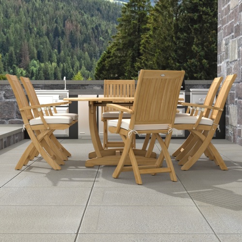 70368 Oval Barbuda Chair 7 pc Dining Set of Martinique Oval Table and 6 Barbuda Teak Arm Chairs in angled end view on outdoor patio with trees in the background