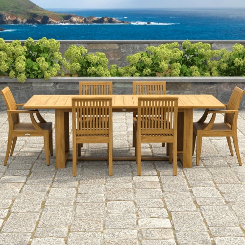 70377 Horizon Laguna 7 pc Teak Dining Set of Horizon Dining Table and 2 Laguna DIning Arm Chairs and 4 Side Chairs on paver patio with landscaping plants and ocean and cliffs in the background