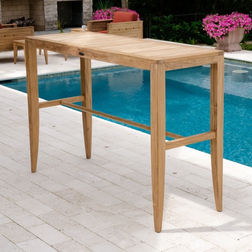 70647 Somerset Laguna teak rectangular table angled on pavers next to pool with 2 flowering plants fireplace and shrubs in background