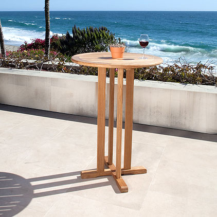 70681 Somerset teak round 30 inch bar table on concrete terrace with plant and glass of wine on table patio surrounded by landscape plants with ocean and blue sky in background