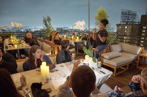 11800DP Maya Slipper Chair set rooftop seating area with pillar candles and potted orchid plants and people sitting around while clapping with night sky in background