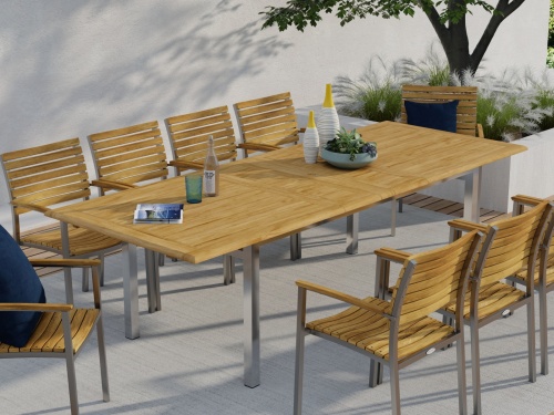 25025 Vogue Extension Table and 9 Vogue Side Chairs angled side view in front of wall on outdoor patio next to a planter box with a tree and landscaping plants in background