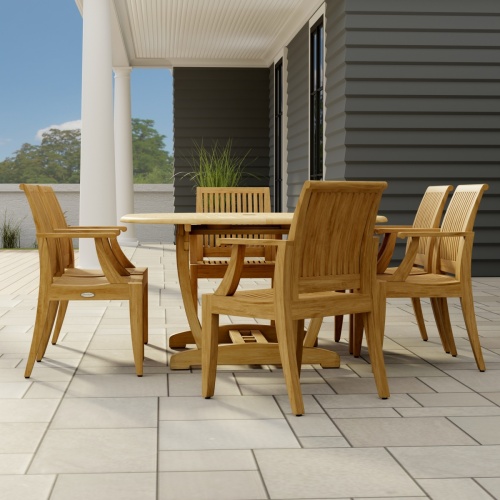 70306 Martinique 7 pc Teak Dining Set of Martinique Teak Oval Extending Dining Table and 6 Laguna DIning Chairs end view on stone patio with 2 pillars of house with a plant and trees and privacy wall in the background  