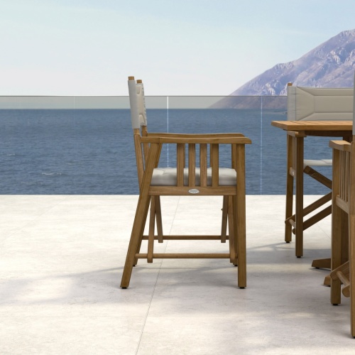 70360 Pyramid Director Chair with teak protector finish side view on stone patio with ocean and land mass in background 