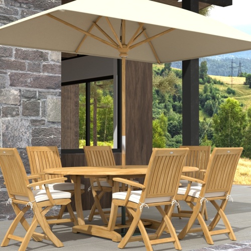 70368 Oval Barbuda Chair 7 pc Dining Set of Martinique Oval Table with umbrella and 6 Barbuda Teak Arm Chairs in angled end view on outdoor patio with trees and ocean background 