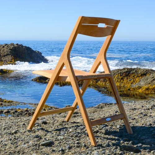 70472 Surf Nevis teak folding side chair left side view on beach facing ocean and blue sky