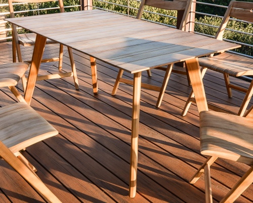  70552 Vogue Surf teak 5 foot rectangular dining table closeup view of dining table on wood deck with plants in background