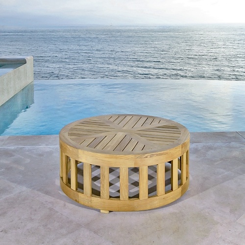 14171 Kafelonia 36 inch Round Teak Coffee Table angled on stone patio in front of pool with ocean and blue sky in background 