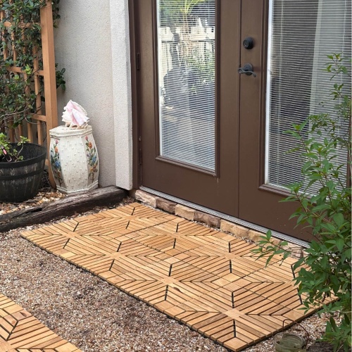 18408P diamond teak tiles showing 8 on rocks assembled together in front of French doors with landscaping ornaments and plants in background 