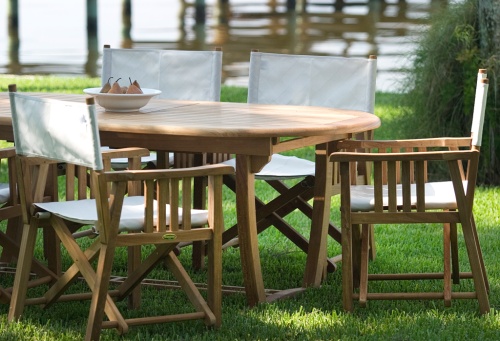 70015 Montserrat Director 9 piece teak Dining Set with white bowl of pears on grass lawn with boat dock and lake background