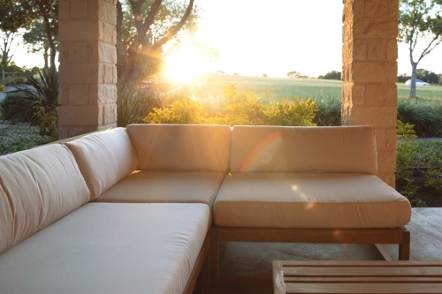 13801dp maya sectional collection on patio surrounded by landscape plants with view of grassy field with sunset in background 