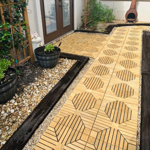 18408P diamond teak tiles assembled on a walkway leading to a door with landscaping rocks and plants on each side and chimenea against a wall in background 