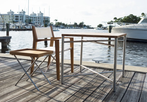 25815 Odyssey Teak and Stainless Steel 32 Inch Square Outdoor Folding Table and 4 Odyssey Chairs  side angled view on a dock with lake and natural vegetation in the background