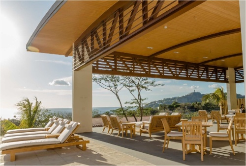 70292 Pyramid Laguna 5 piece teak Dining Set on concrete patio under a covered pavilion at Santa Maria Nicaragua Resort with ocean view and hills and blue sky background