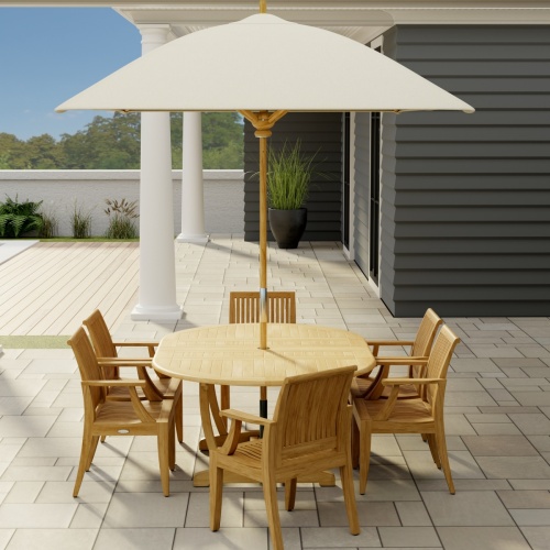 70306 Martinique 7 pc Teak Dining Set with optional rectangular umbrella in end view on stone patio with 2 pillars of house and a potted plant a privacy wall and trees in the background