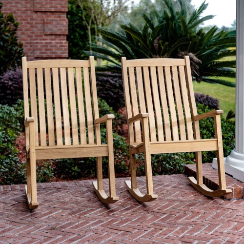 12223 two veranda teak rocking chair front view on brick porch with railing plants and trees in background