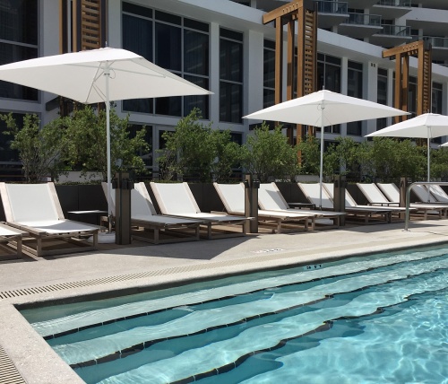 70939 Maya Teak Sling Lounger in white textilene mesh fabric showing 11 loungers next to pool with hotel in background