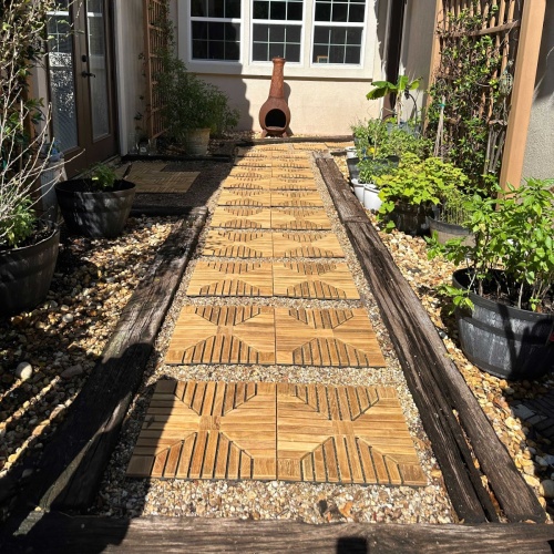  18408P diamond teak tiles installed on a walkway surrounded with landscaping plants and 2 trellises with chimenea and house in background  