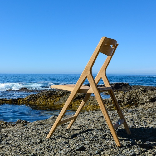 11916 Surf Teak Folding Side Chair on sand facing ocean with rocks ocean and blue sky in background